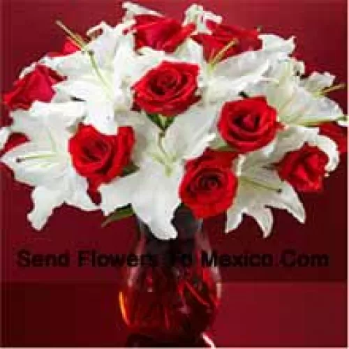 Roses rouges et lys blancs avec quelques fougères dans un vase en verre